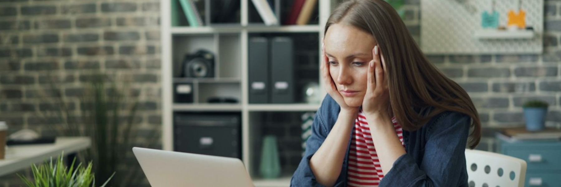 A woman sitting at a laptop with her head in her hands